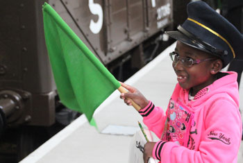 Picture of young school girl dressed as a railway conductor and waving a flag on a school trip to a railway museum