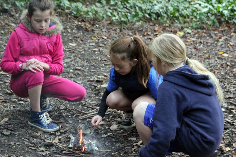 Picture of school girls lighting fire in woods to reference bushcraft activity school trips